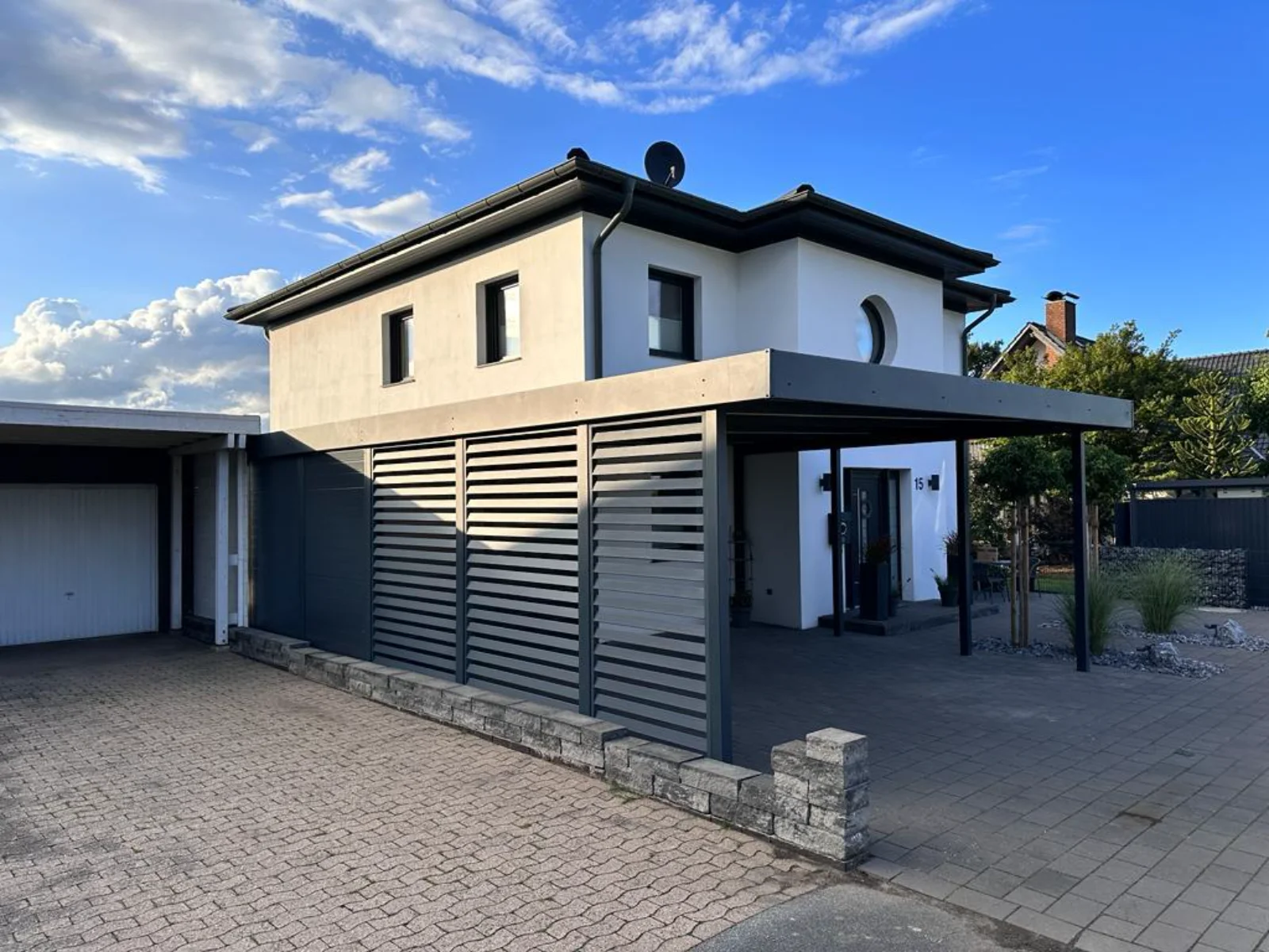 Modernes Carport mit Metall-Sichtschutzlamellen vor zweistöckigem Wohnhaus