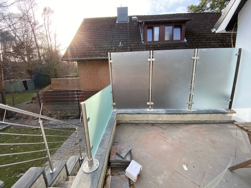 Balkon mit Glasgeländer aus Edelstahlpfosten und satiniertem Glas auf steinerner Terrasse
