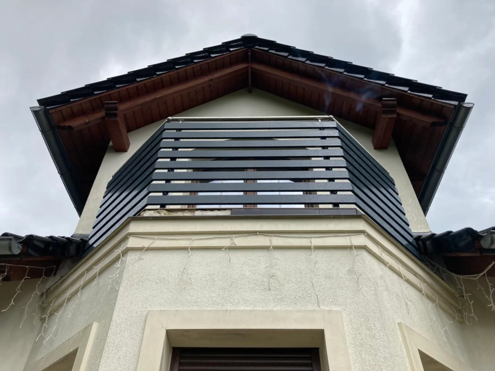 Schwarzes Metallgeländer mit waagerechten Latten an vorgelagertem Balkon vor weißer Fassade