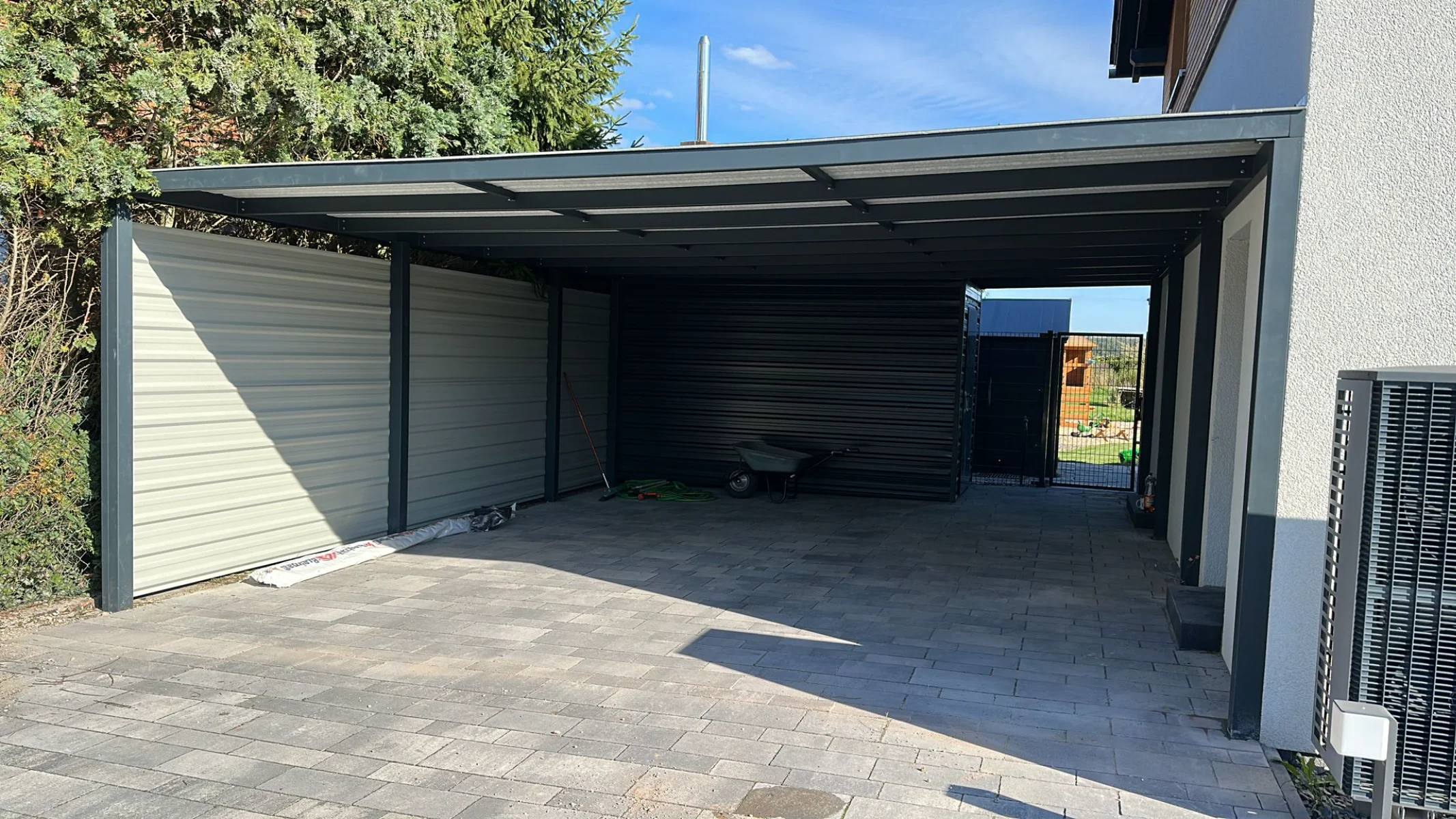 Überdachtes Carport aus pulverbeschichtetem Metall mit seitlichen Blechwänden auf Pflasterfläche