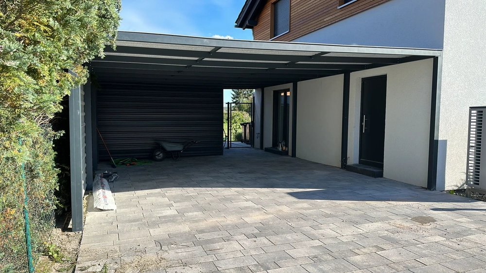 Moderner anthrazitfarbener Carport mit Flachdach vor Einfamilienhaus auf gepflasterter Auffahrt