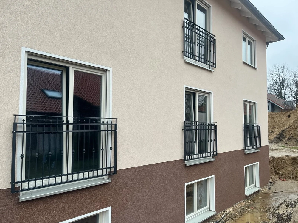 Fassadenansicht eines Gebäudes mit schwarzen Fenstergeländern und Balkonbrüstungen