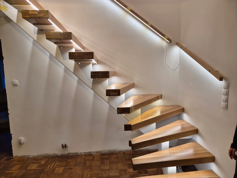 Freitragende Holztreppe mit keilförmigen Stufen und integrierter LED-Beleuchtung an einer weißen Wand