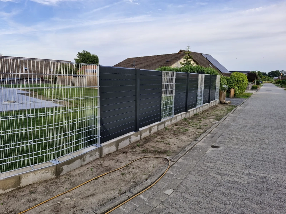 Doppelstabmattenzaun mit anthrazitfarbenen Sichtschutzlamellen auf Betonfundament neben gepflastertem Gehweg