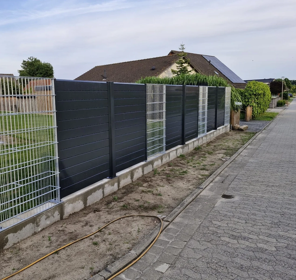 Moderner Metallzaun als Kombination aus blickdichten Alu-Paneelen und Gitterelementen auf Betonsockel