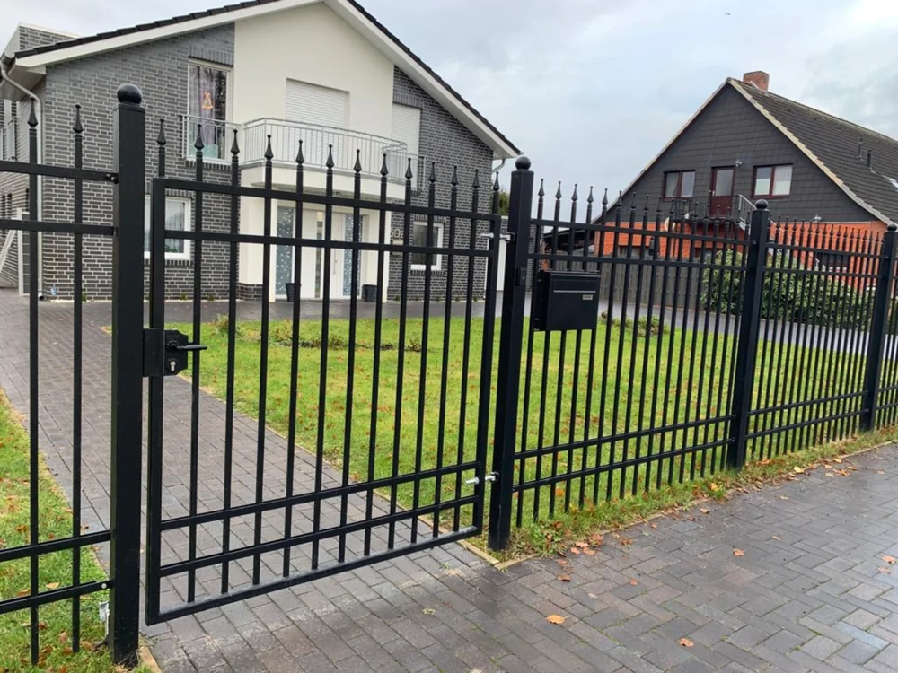Schwarzer Metallzaun mit Tor und Briefkasten vor modernem Einfamilienhaus und Vorgarten