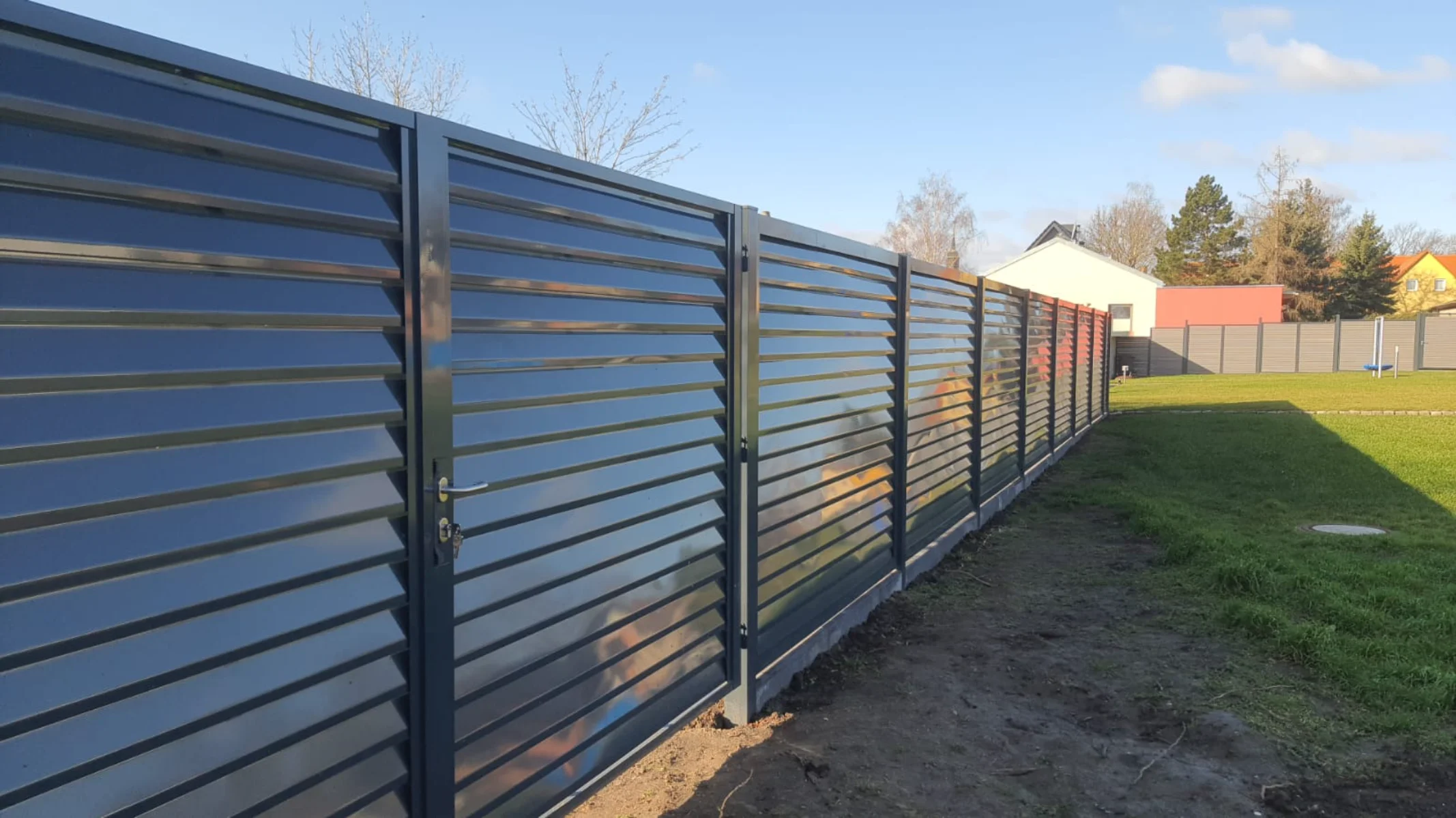 Metallzaun mit waagerechten Lamellen und integriertem Tor vor Rasenfläche