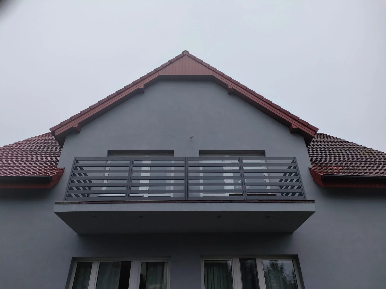 Moderner Balkon an grauer Fassade mit maßgefertigtem Metallgeländer und rotem Ziegeldach