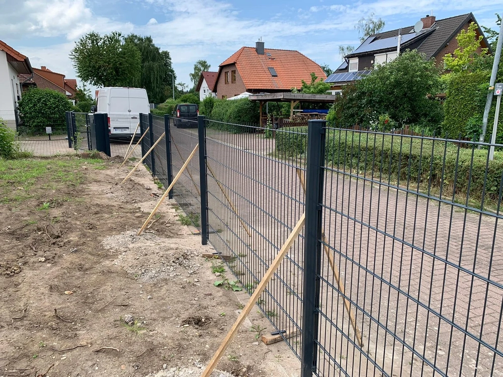 Neu montierter Doppelstabmattenzaun mit Abstützung entlang eines gepflasterten Wegs vor Einfamilienhäusern
