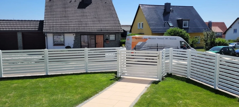 Weißer Metallzaun mit horizontalen Lamellen und Gartentor vor gepflegtem Rasen und Einfamilienhäusern