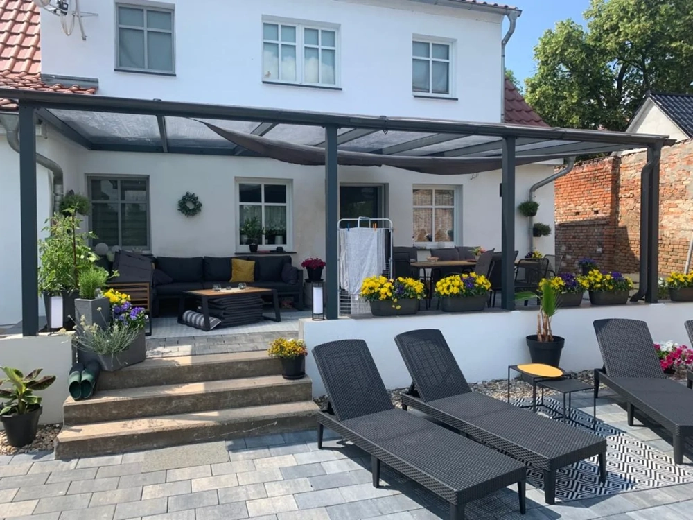 Terrassenüberdachung aus Metall mit gemütlichen Lounge-Möbeln und Sonnenliegen auf gepflasterter Terrasse