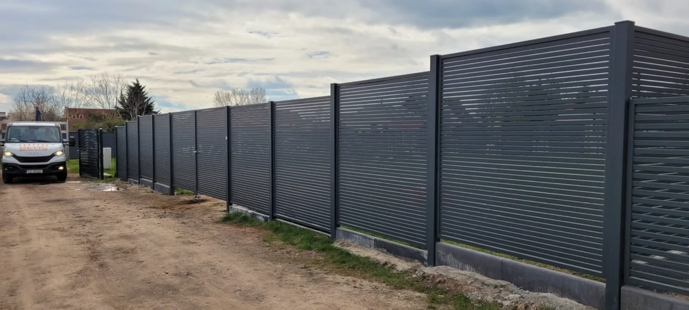 Moderner anthrazitfarbener Metallzaun aus horizontalen Lamellen entlang eines Schotterwegs