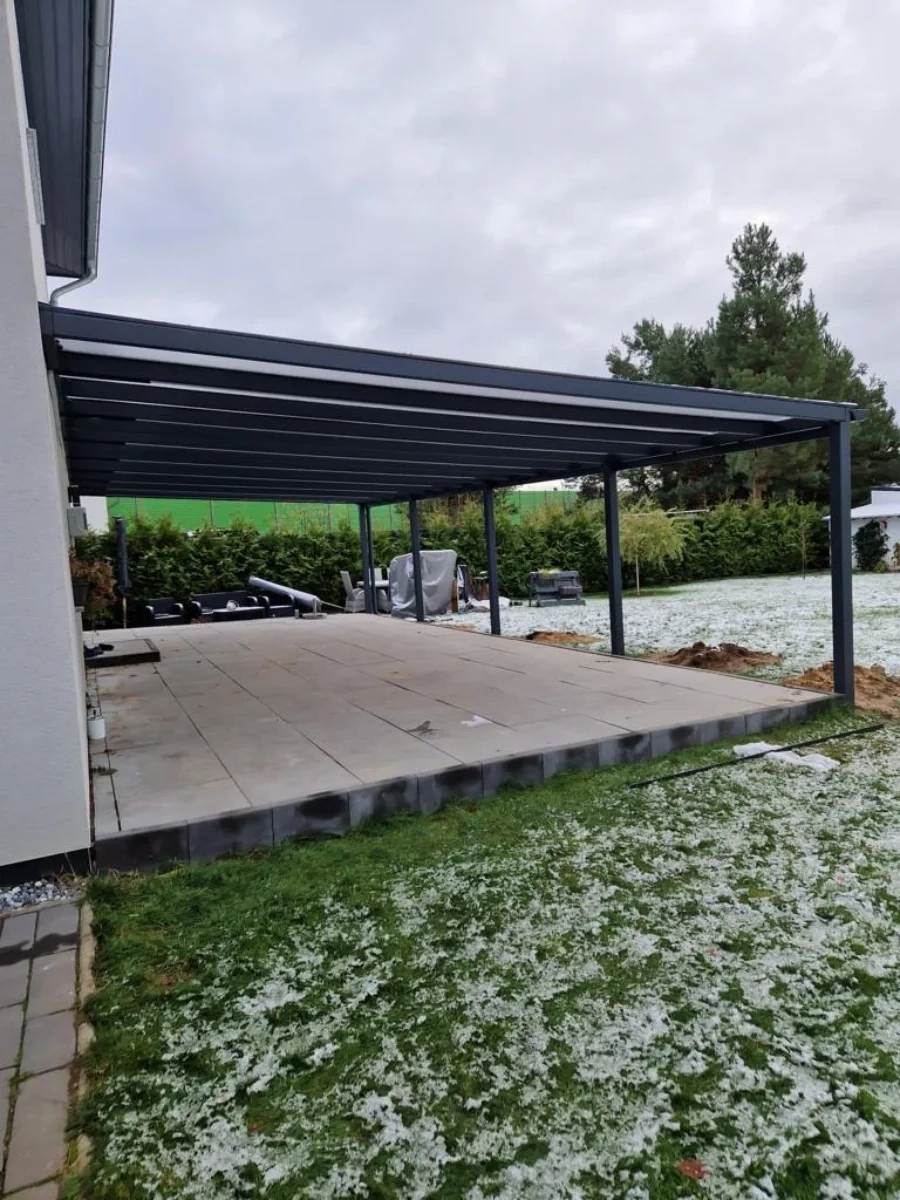 Moderne Terrassenüberdachung aus pulverbeschichtetem Stahl über großflächiger Platten-Terrasse mit leichtem Schneebelag