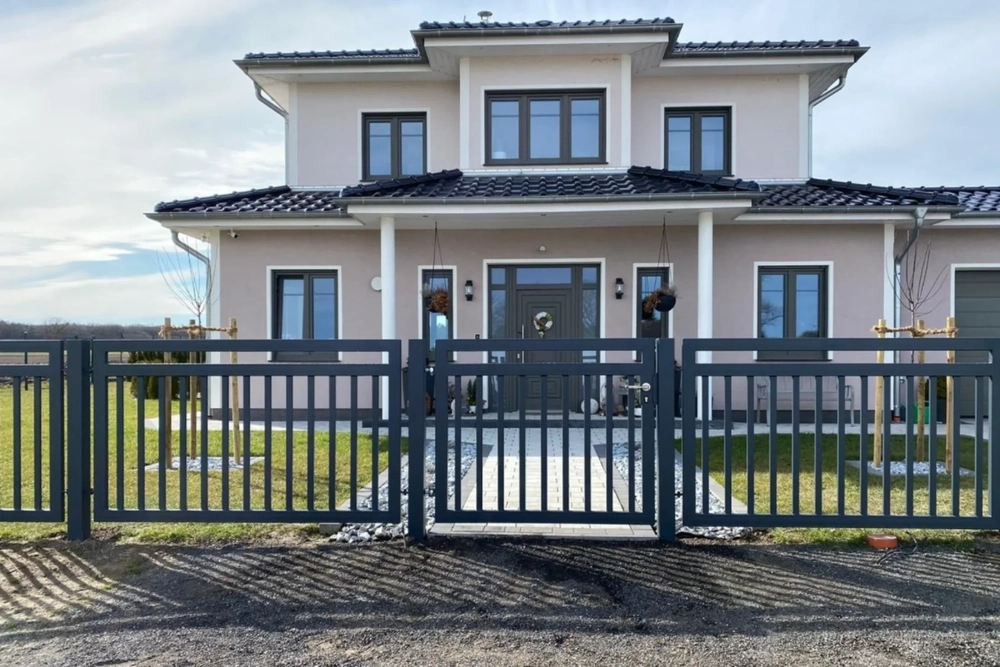 Pulverbeschichteter Metallzaun mit Einfahrtstor vor modernem Einfamilienhaus und gepflegtem Vorgarten