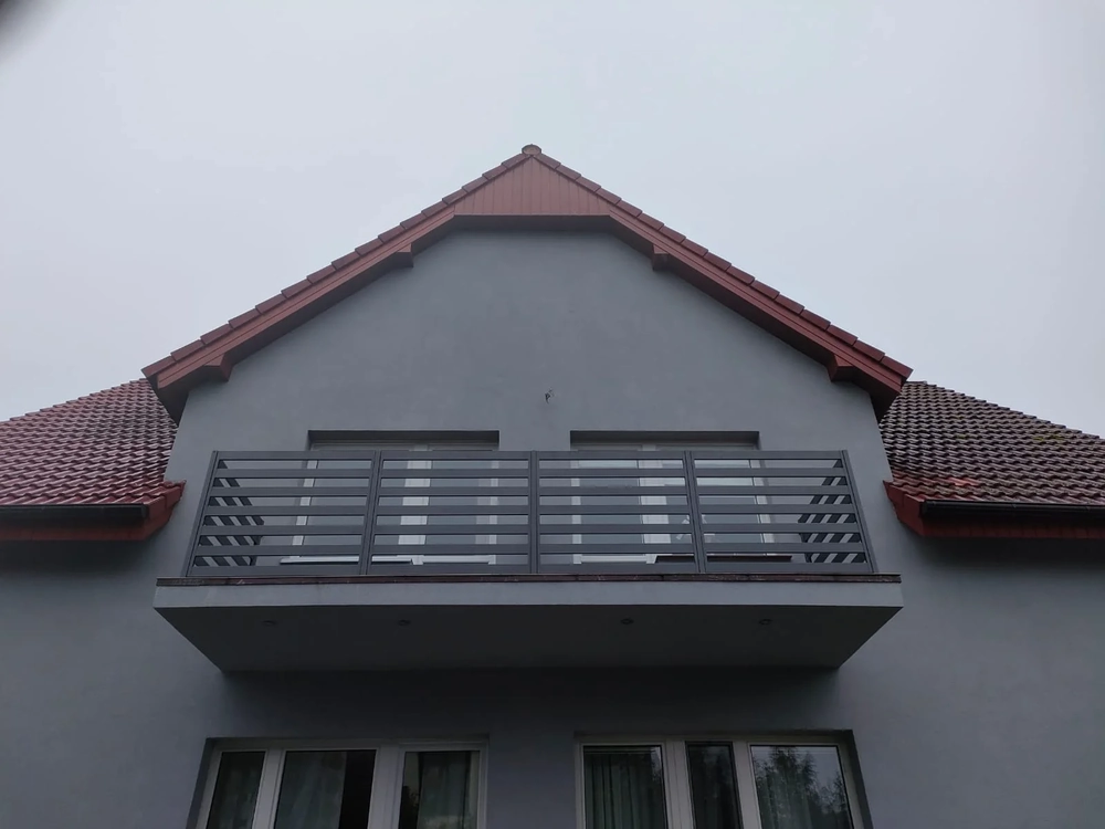 Modernes Balkongeländer aus dunklem Metall mit horizontalen Lamellen an grauer Fassade
