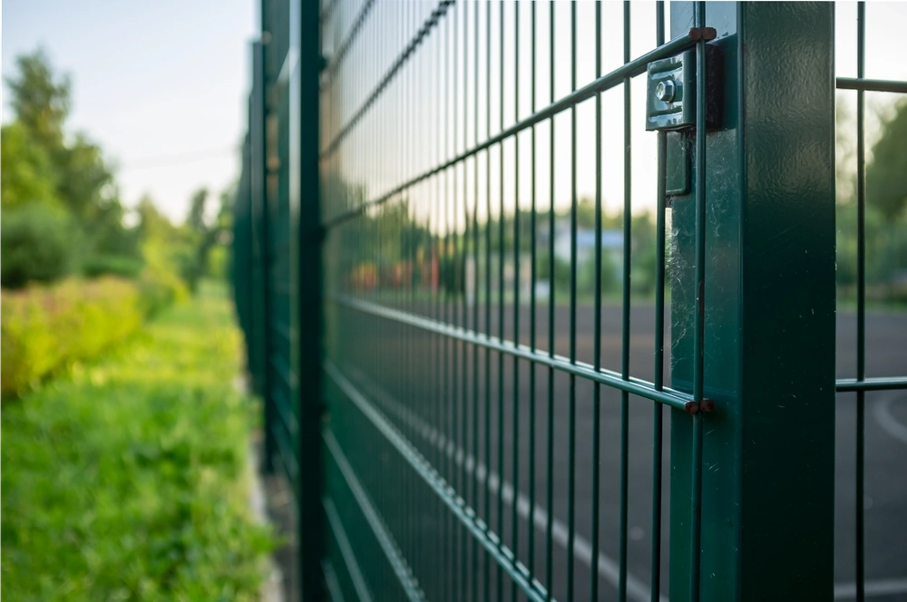 Nahaufnahme eines grünen Doppelstabmattenzauns mit Metallpfosten neben einem Grasweg