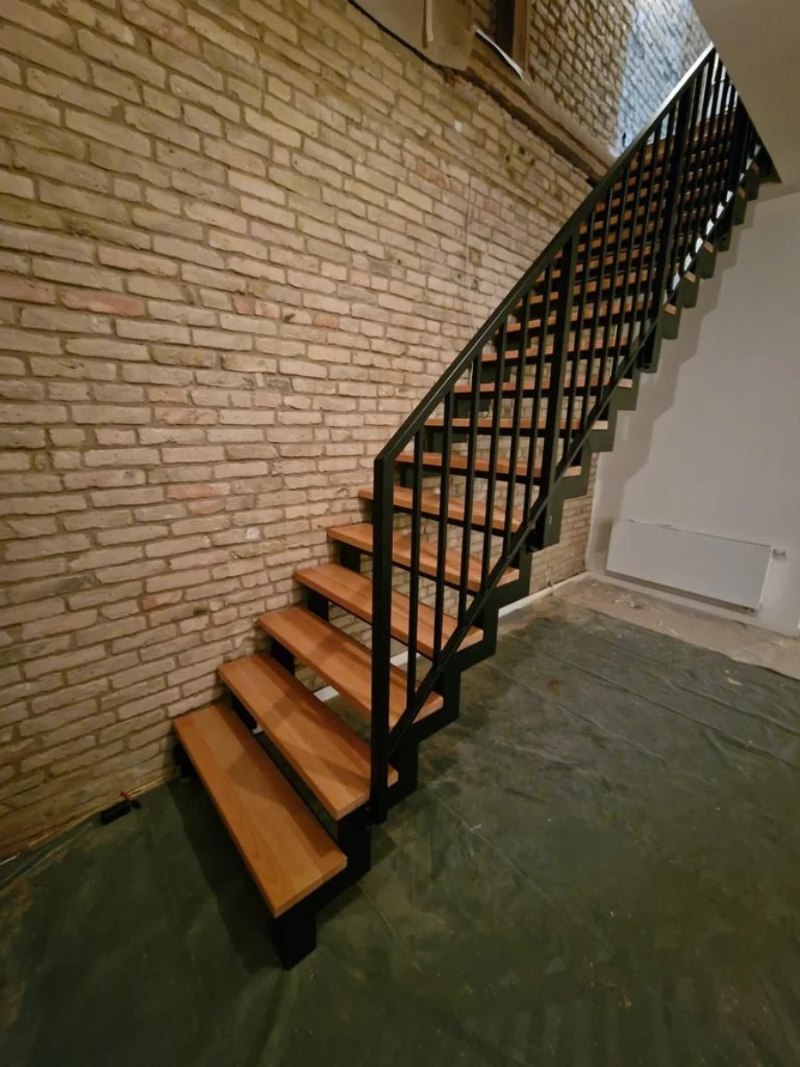 Treppe mit Holzstufen und pulverbeschichtetem Metallgeländer vor freigelegter Ziegelsteinwand