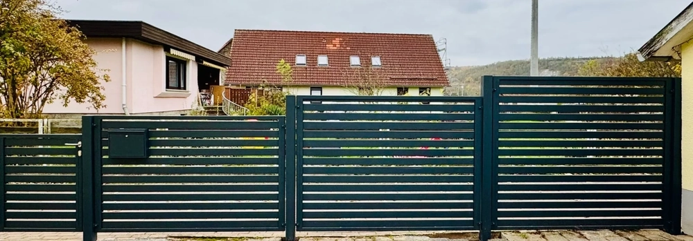 Anthrazitfarbener Metallzaun mit horizontalen Lamellen und Einfahrtstor vor Wohnhaus