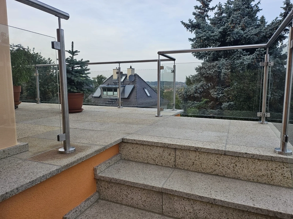 Modernes Edelstahl-Glas-Terrassengeländer auf heller Steinterrasse mit Treppe und Topfpflanzen