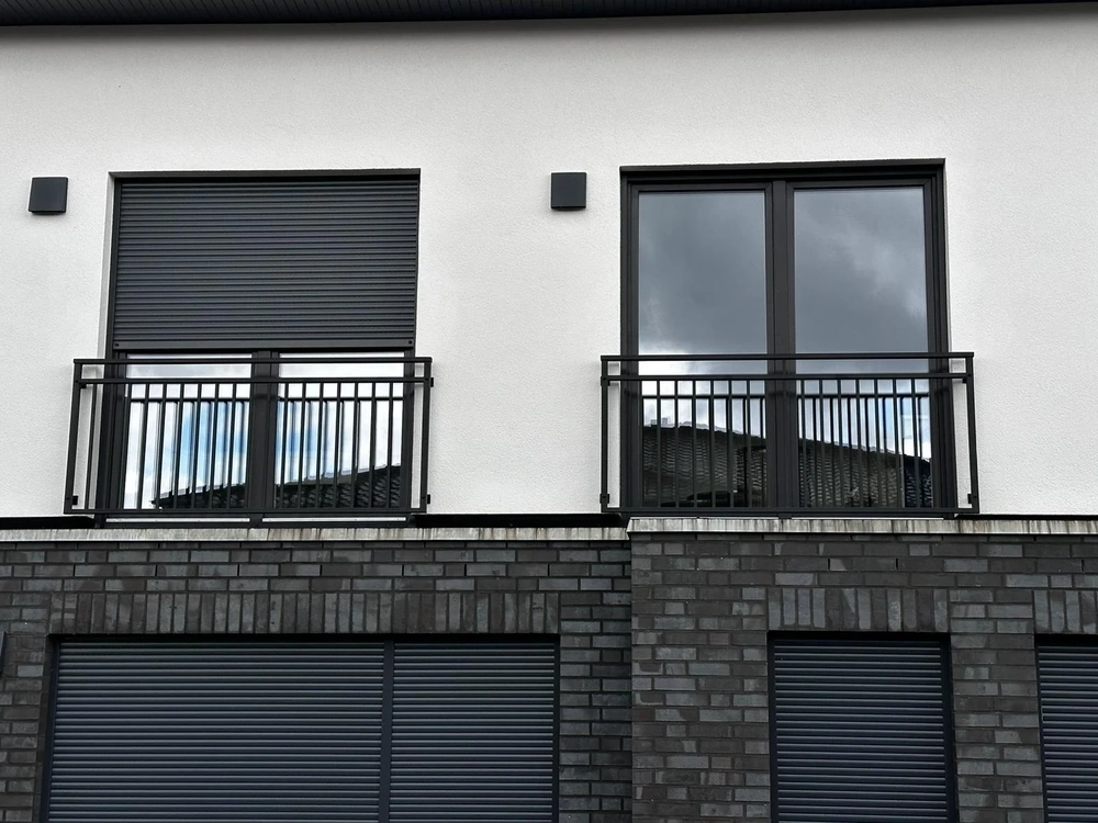 Weiße Hausfassade mit bodentiefen Fenstern und schwarzen Metall-Geländern