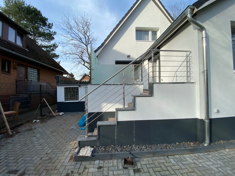 Außentreppe aus Beton mit Edelstahl-Geländer vor modernem Wohnhaus auf gepflasterter Auffahrt